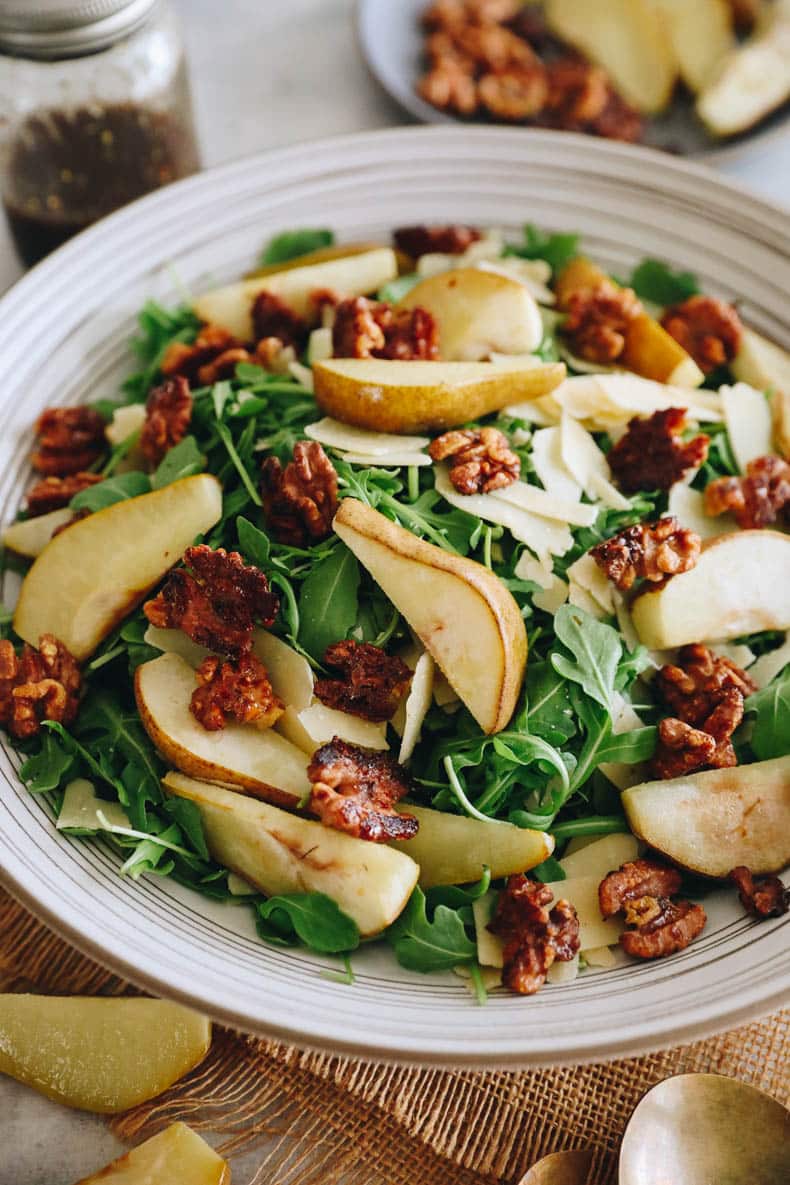 Roasted pear salad with candied walnuts and parmesan over a bed of arugula in a large white salad bowl.