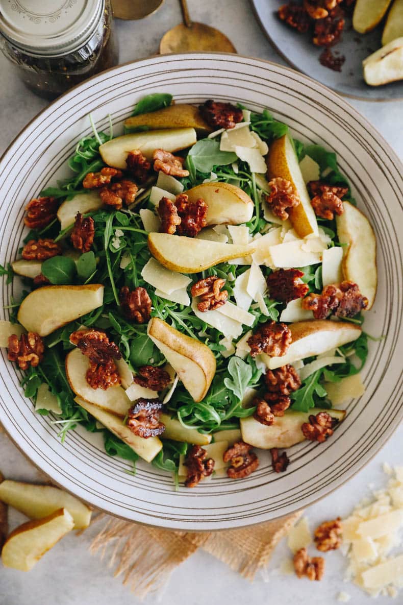 Roasted pear salad in a large white salad bowl with candied walnuts, parmesan and balsamic dressing.