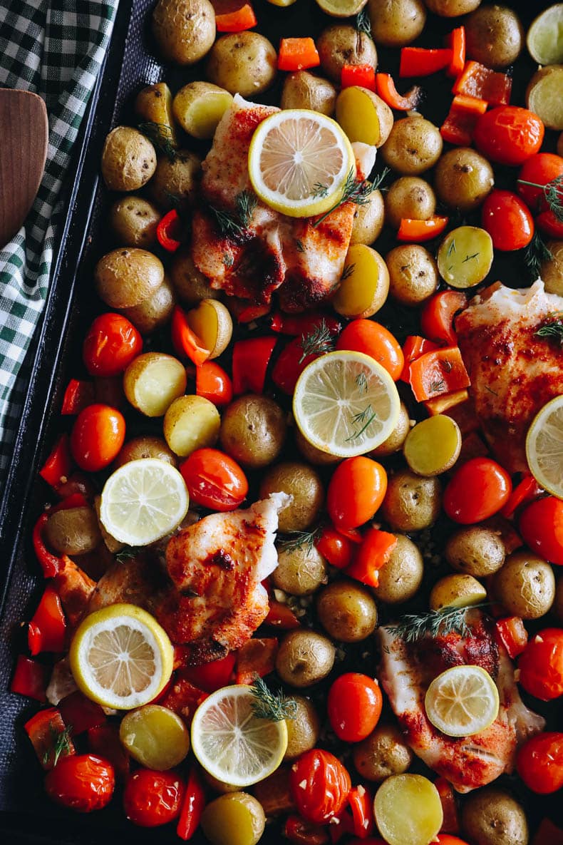 overhead image of baked cod on a sheet pan with veggies, lemon and dill.
