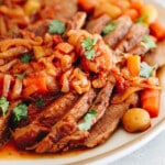 Classic Jewish brisket with caramelized onion, carrots, potatoes and parsley on a white platter.