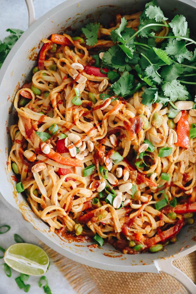 overhead image of rice noodles in a peanut sauce with sriracha, lime, cilantro.