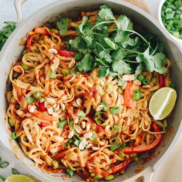 spicy peanut noodles in a pan with cilantro, lime, crushed peanuts and scallions
