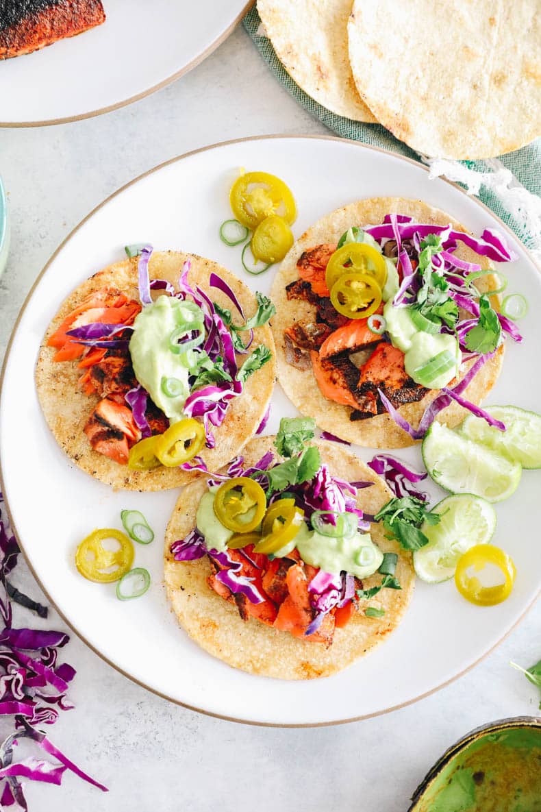 Overhead image of salmon tacos with avocado crema, jalapenos, cilantro, lime and cabbage.