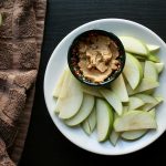 a white plate topped with sliced apples and a bowl of peanut butter
