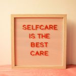 A wooden letter board with red text reading "SELFCARE IS THE BEST CARE"